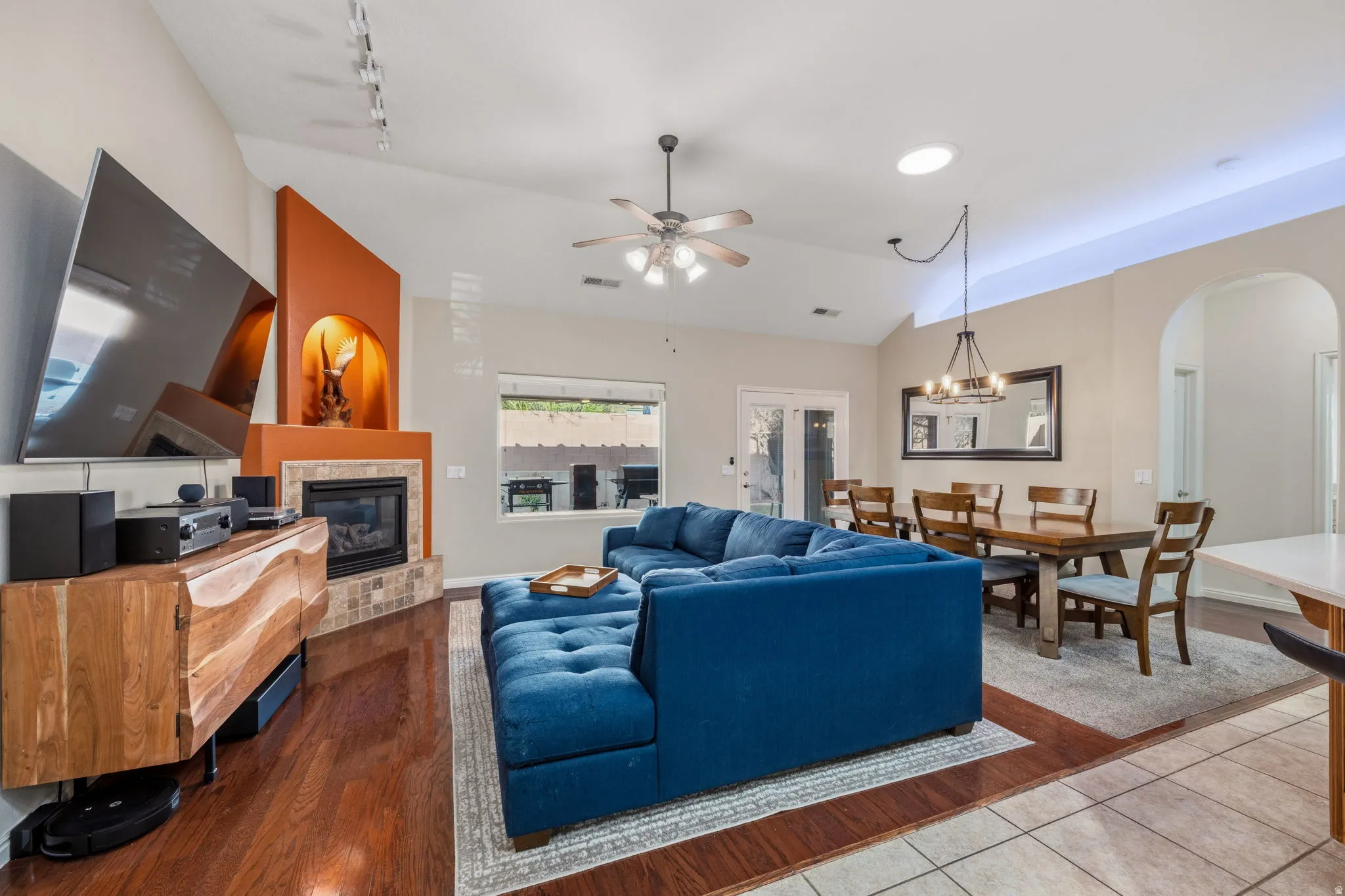 Living area with vaulted ceiling, ceiling fan, a fireplace, hanging lights, and wood finished floors