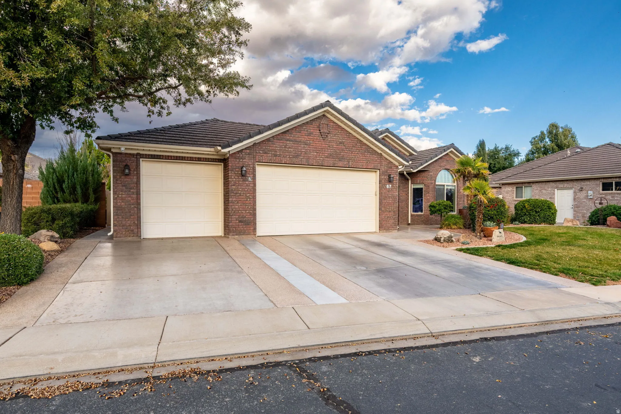 Single story home featuring a garage, a tiled roof, driveway, and brick siding