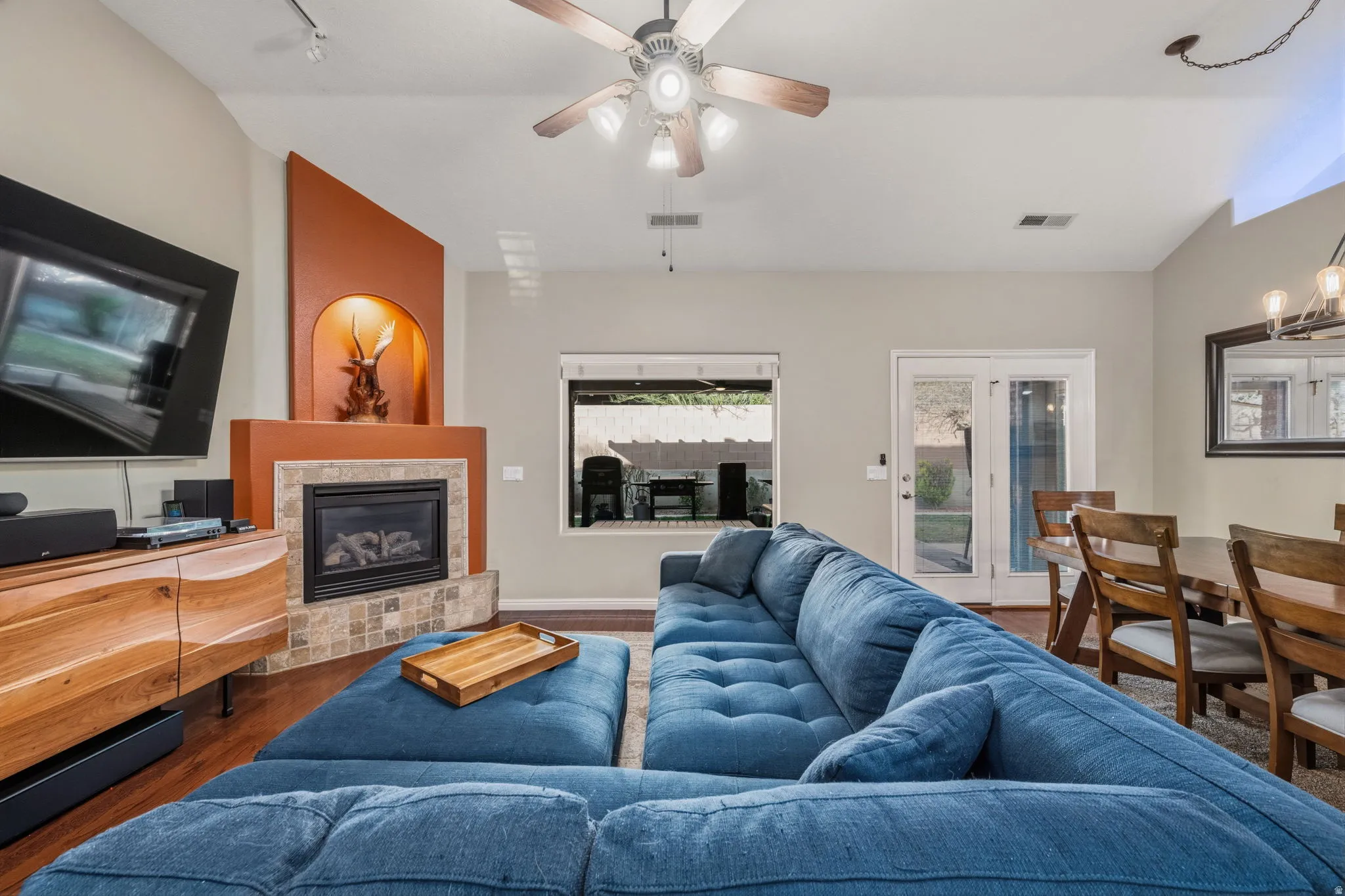 Living room featuring wood finished floors, vaulted ceiling, a tile fireplace, a ceiling fan, and suspended lighting
