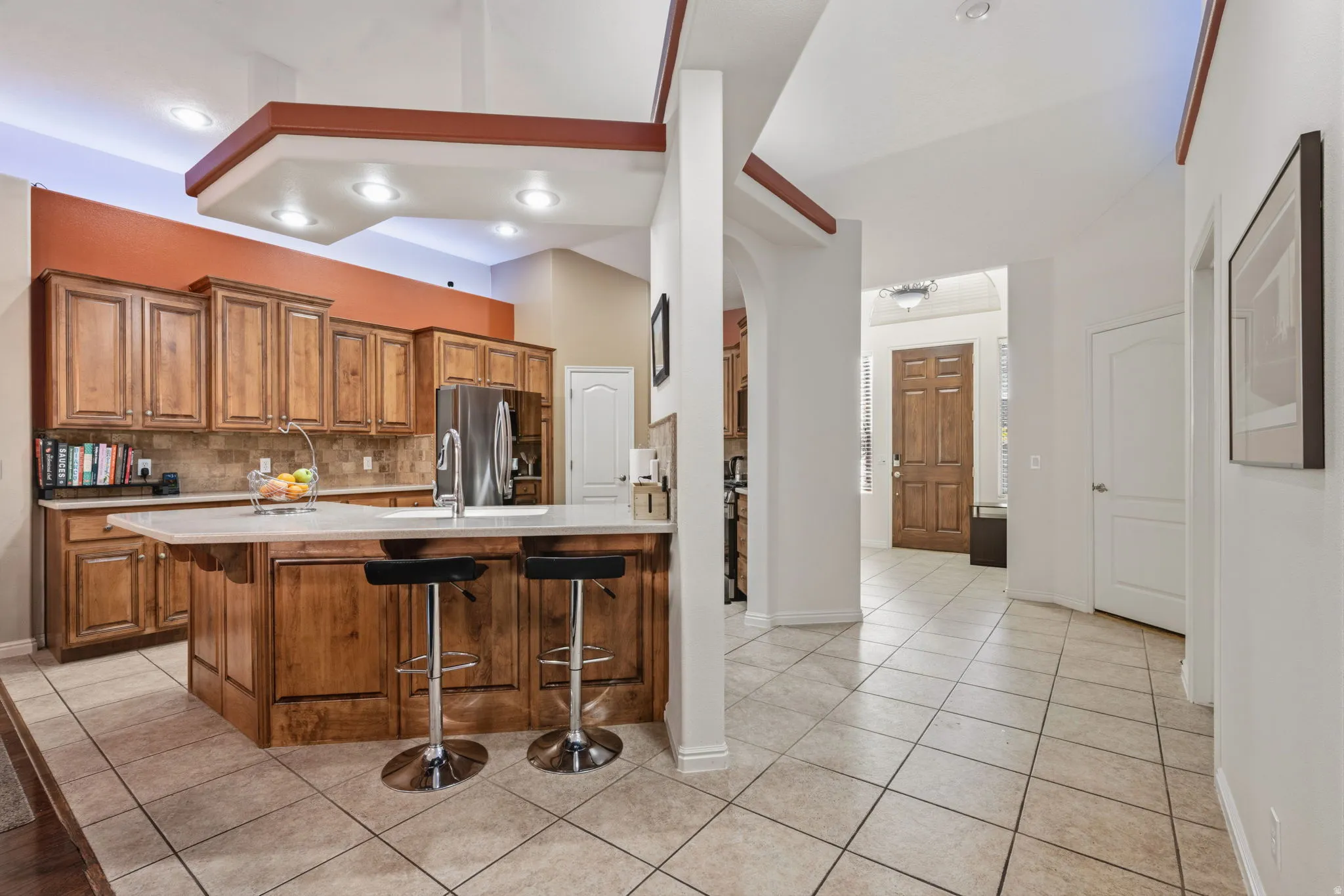 Kitchen featuring wood finish cabinetry, a breakfast bar area, light tile patterned floors, stainless steel fridge, and arched walkways