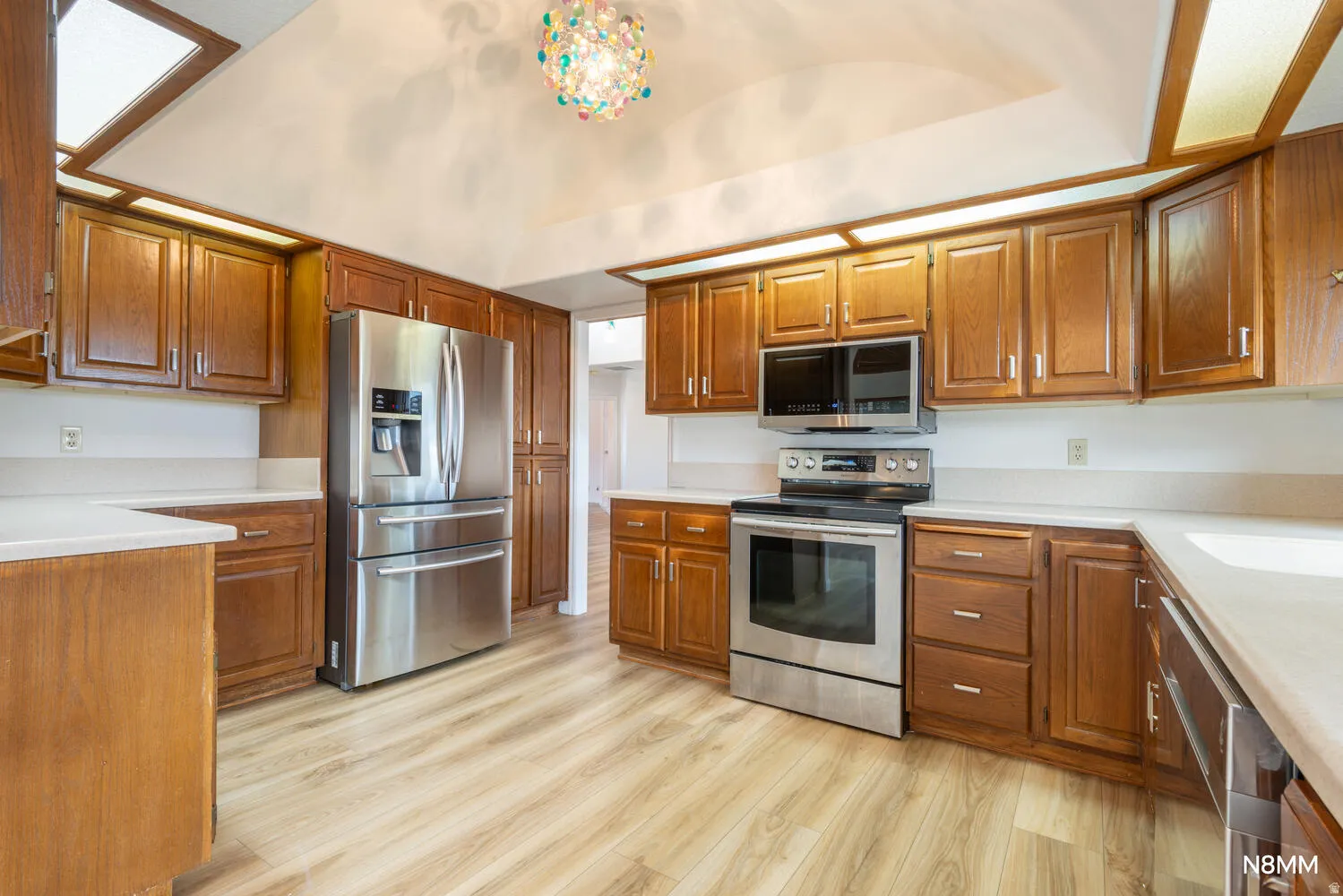Kitchen featuring stainless steel appliances, wood finish cabinets, light wood finished floors, and vaulted ceiling