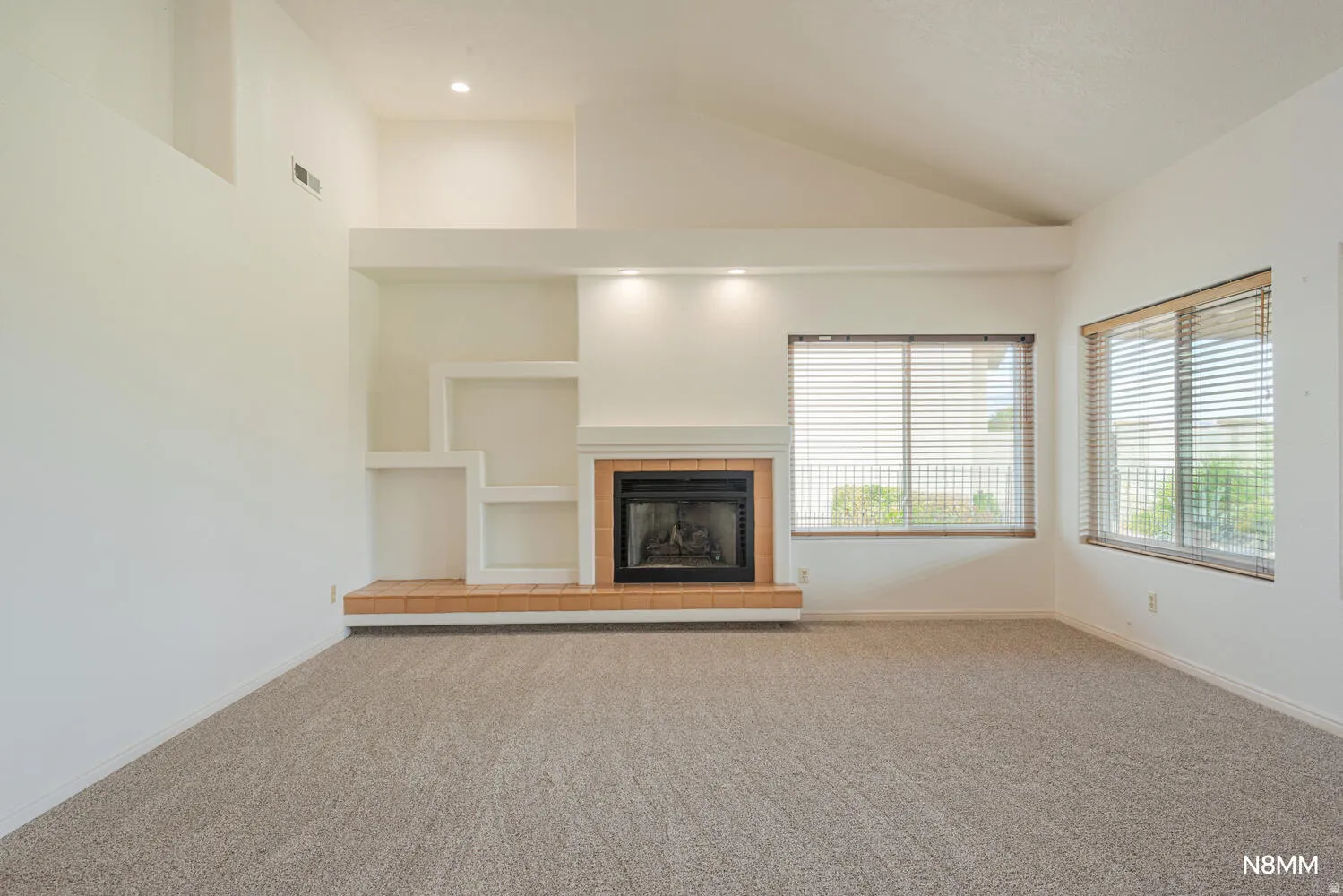 Unfurnished living room featuring built in shelves, a tile fireplace, carpet floors, and vaulted ceiling