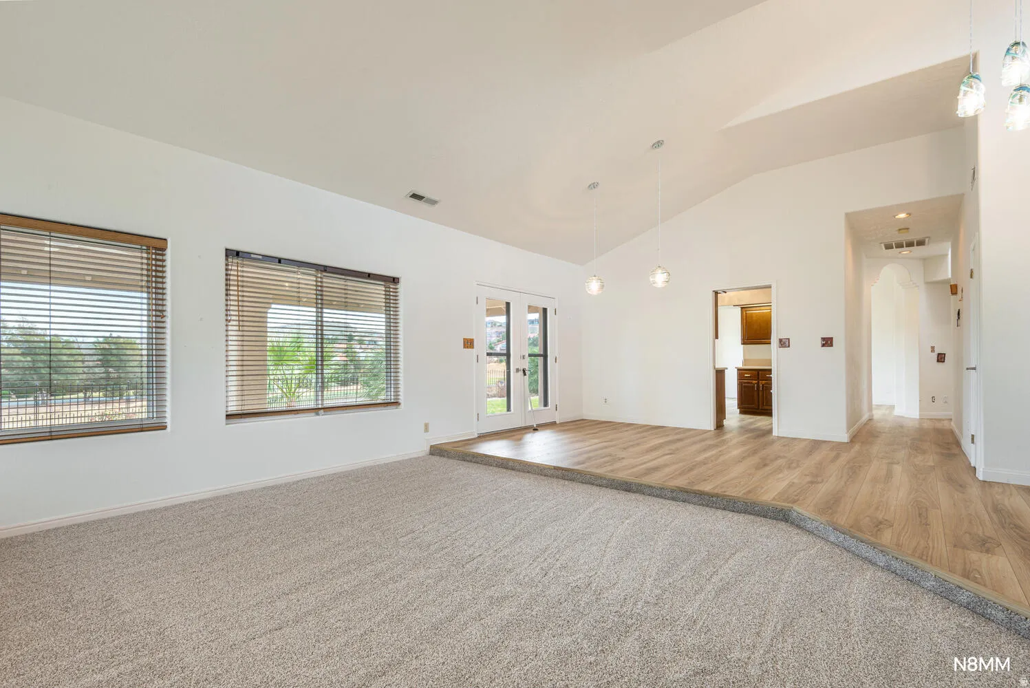 Unfurnished room featuring french doors, arched walkways, light colored carpet, vaulted ceiling, and light wood finished floors