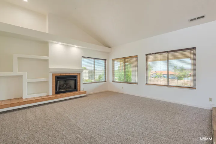 Unfurnished living room with lofted ceiling, carpet floors, and a tiled fireplace
