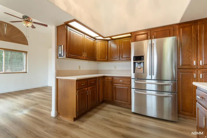 Kitchen featuring stainless steel fridge with ice dispenser, a ceiling fan, light countertops, light wood finished floors, and wood finish cabinets