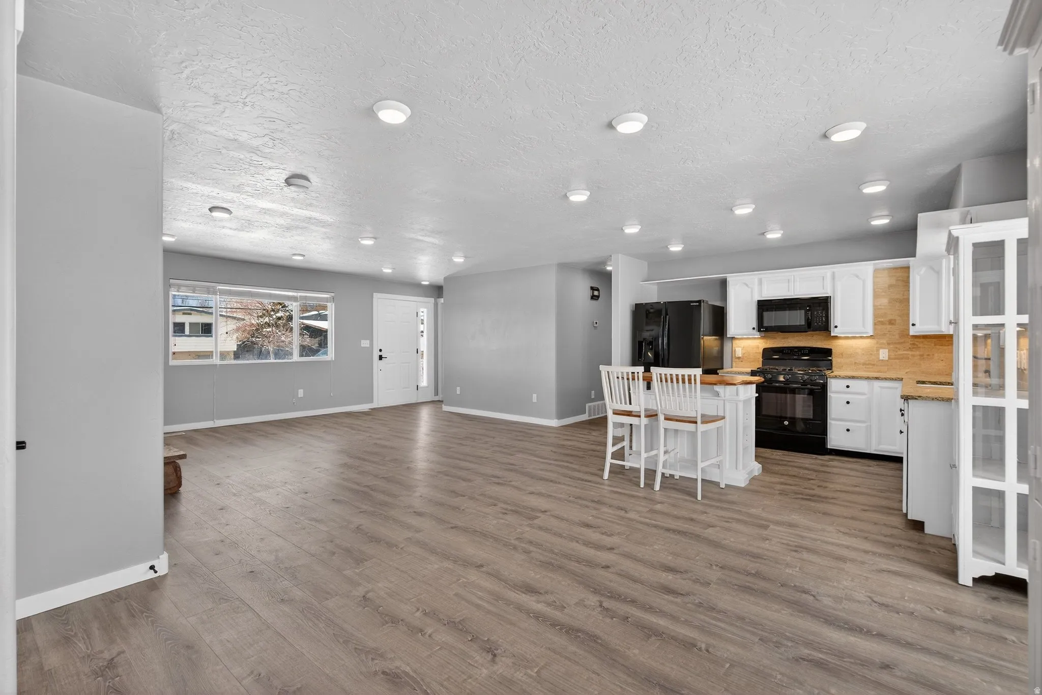 Kitchen featuring a kitchen bar, black appliances, white cabinetry, open floor plan, and light countertops