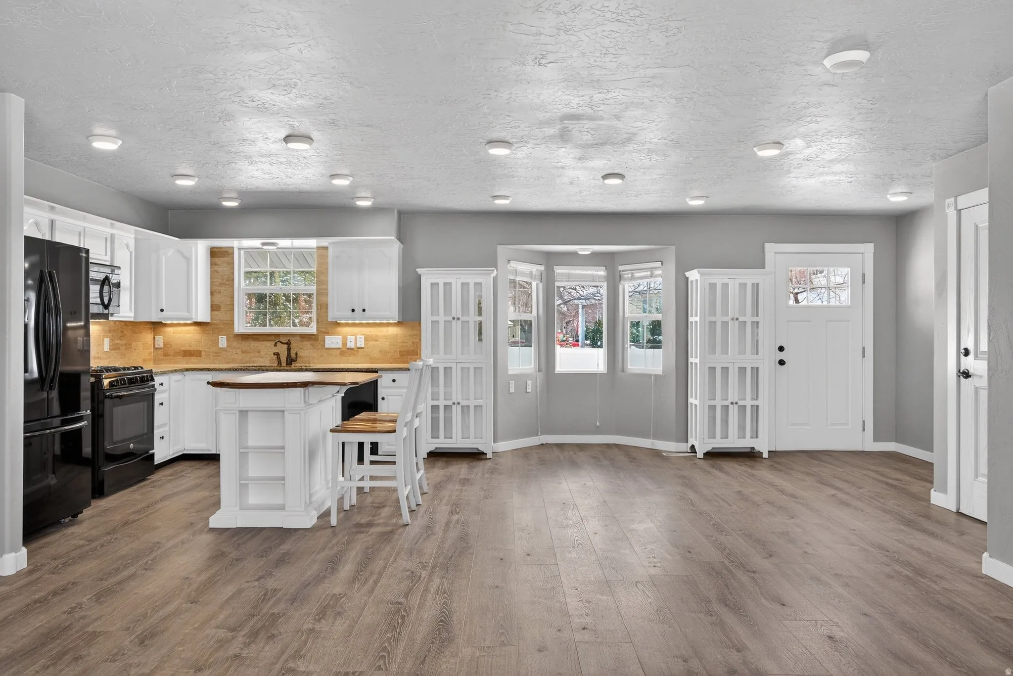 Kitchen with a kitchen bar, white cabinets, black appliances, a center island, and tasteful backsplash