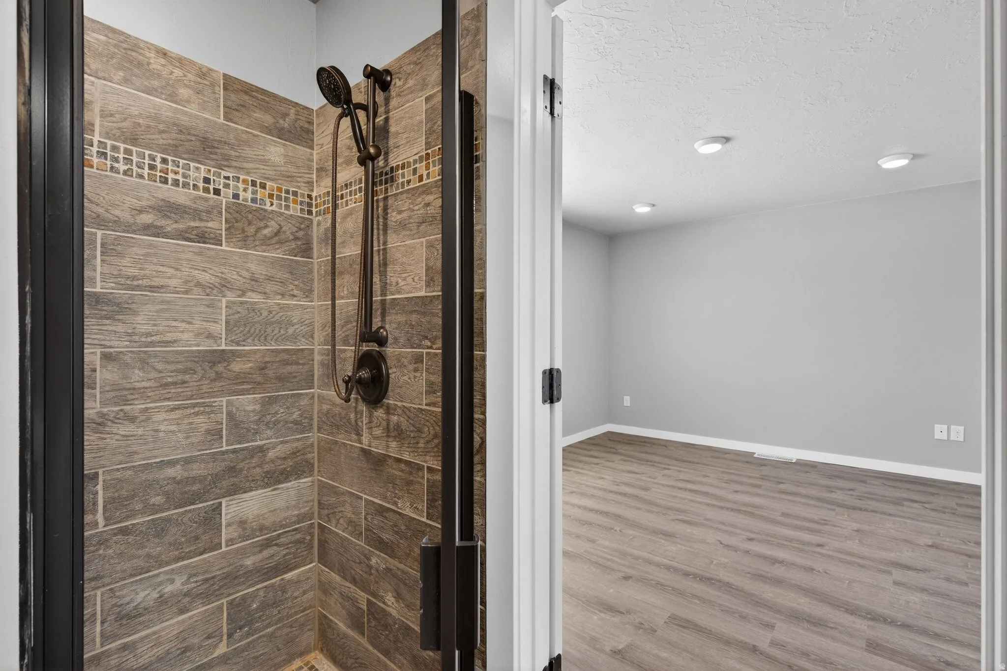 Full bathroom with a shower stall, light wood finished floors, and a textured ceiling