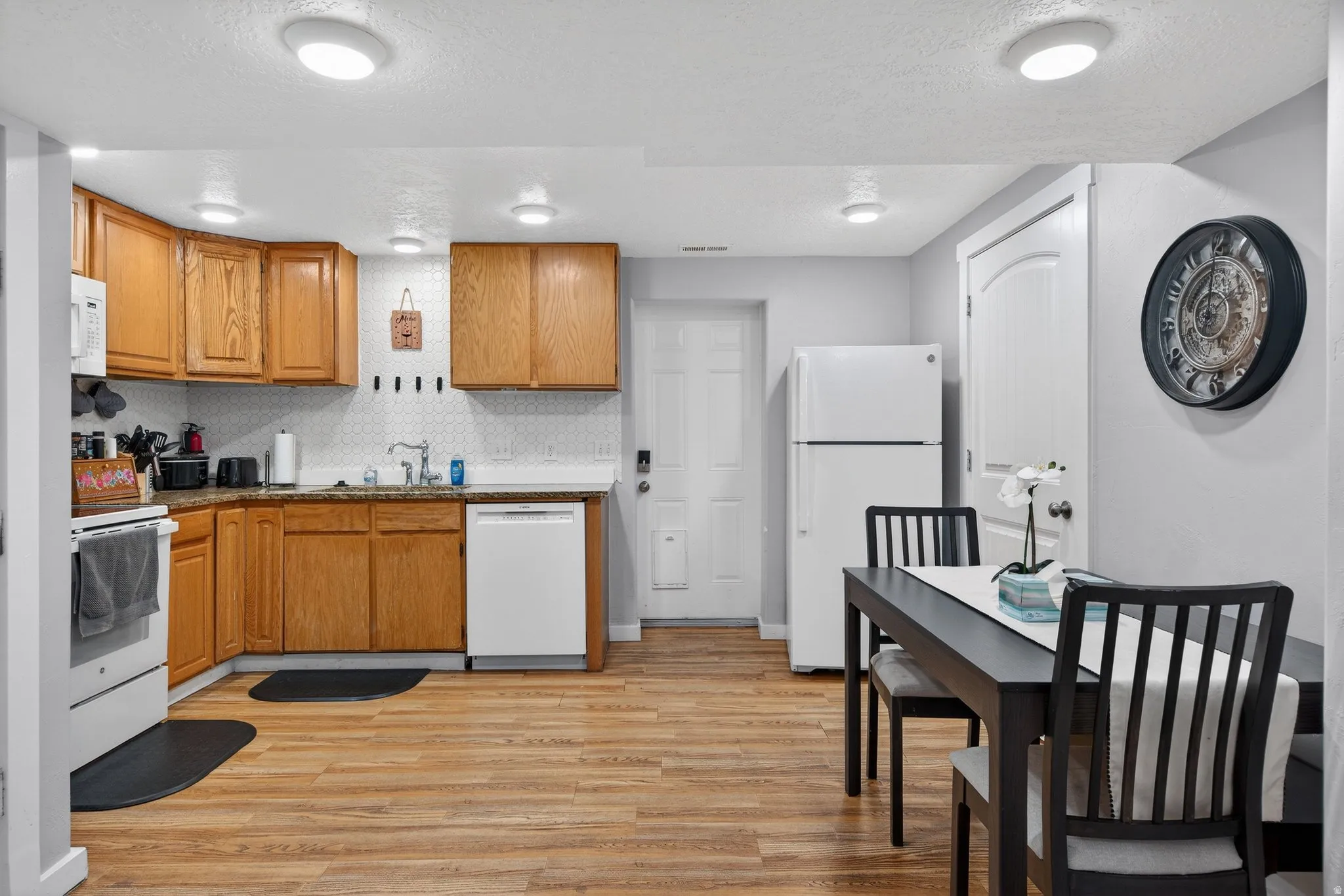 Kitchen with white appliances, wood finish cabinetry, light wood-style flooring, a textured ceiling, and tasteful backsplash