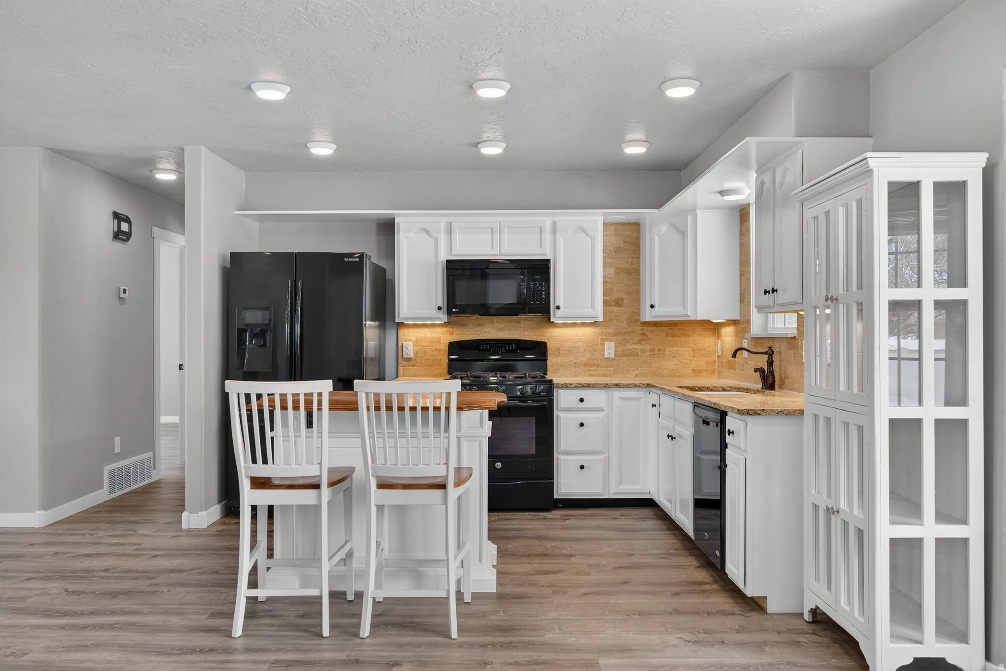 Kitchen featuring a kitchen bar, white cabinetry, black appliances, backsplash, and a textured ceiling