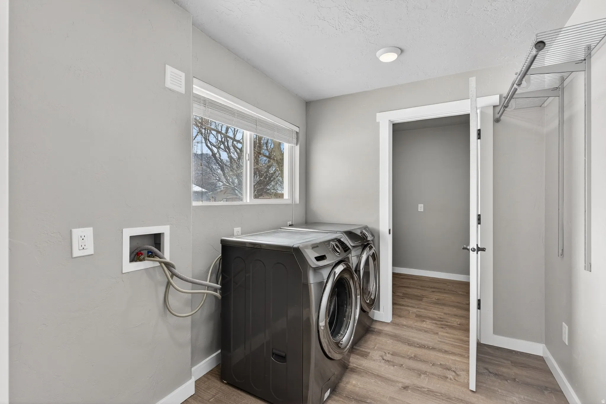 Laundry room with light wood finished floors, a textured ceiling, and washing machine and dryer