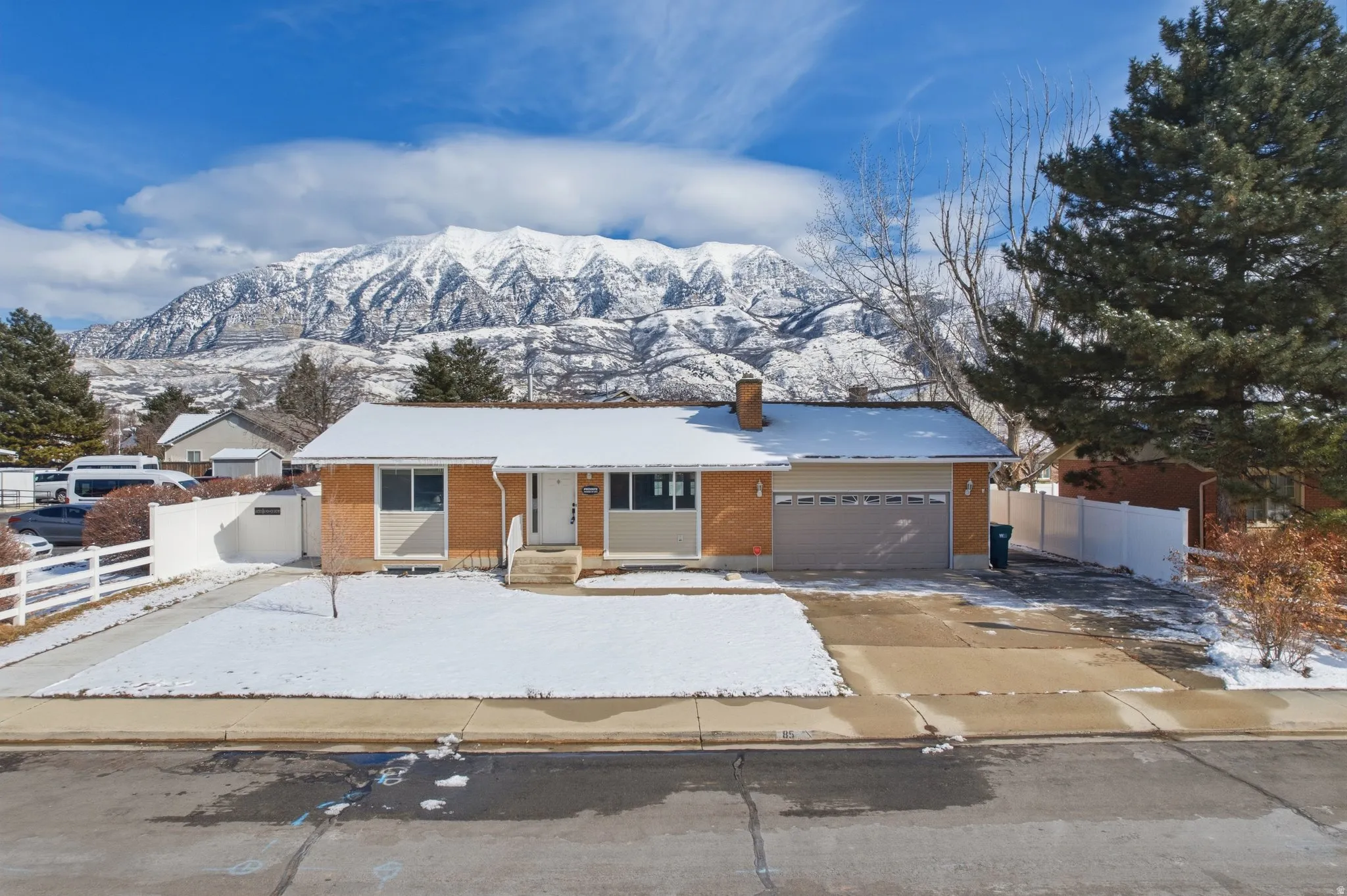 Single story home with brick siding, an attached garage, a chimney, a mountain view, and concrete driveway