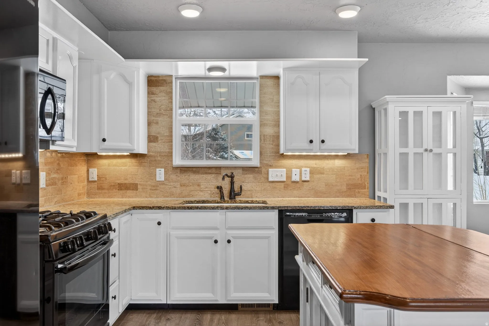Kitchen featuring healthy amount of natural light, black appliances, wood counters, white cabinets, and a textured ceiling