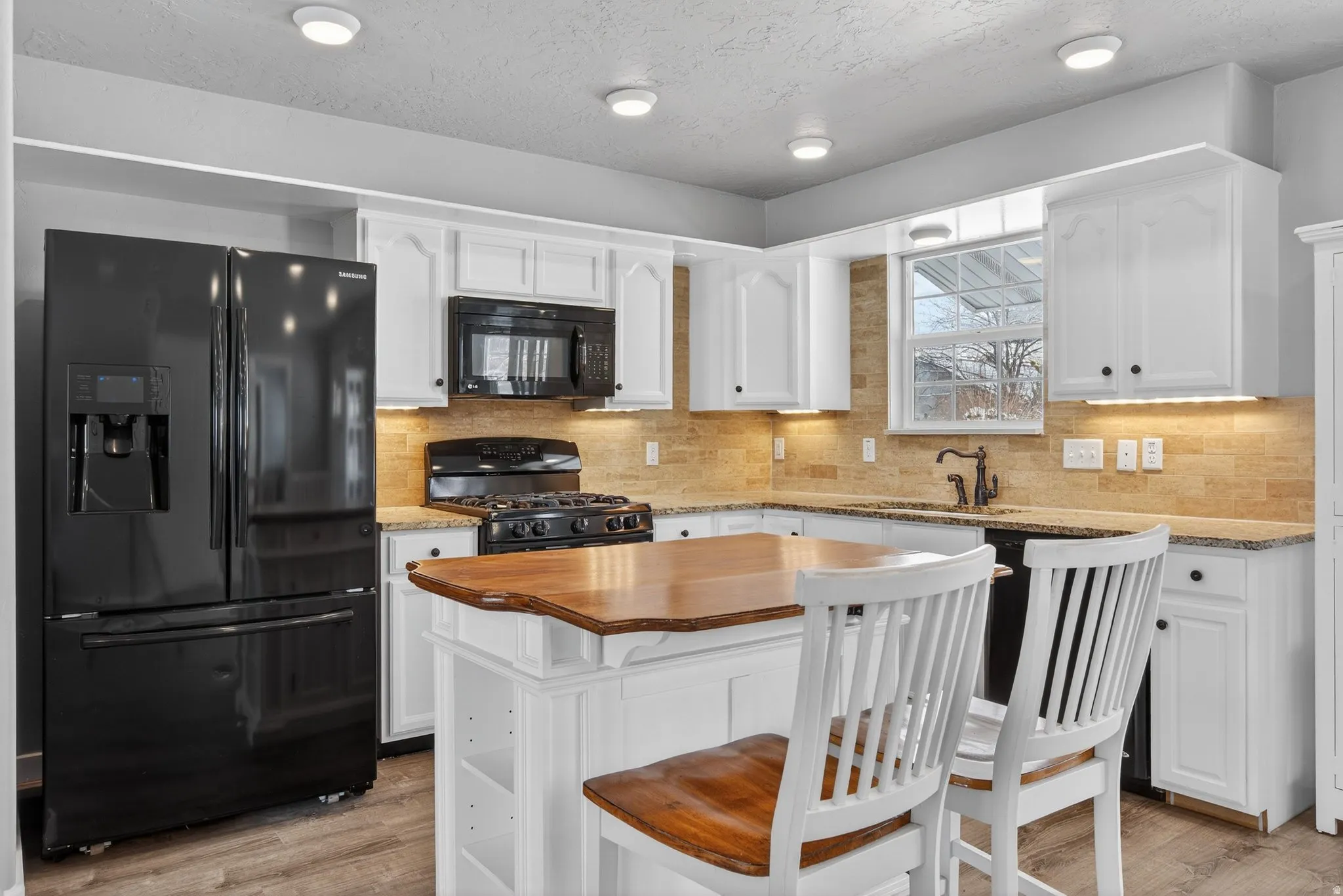 Kitchen with butcher block counters, black appliances, white cabinets, light wood-style floors, and backsplash