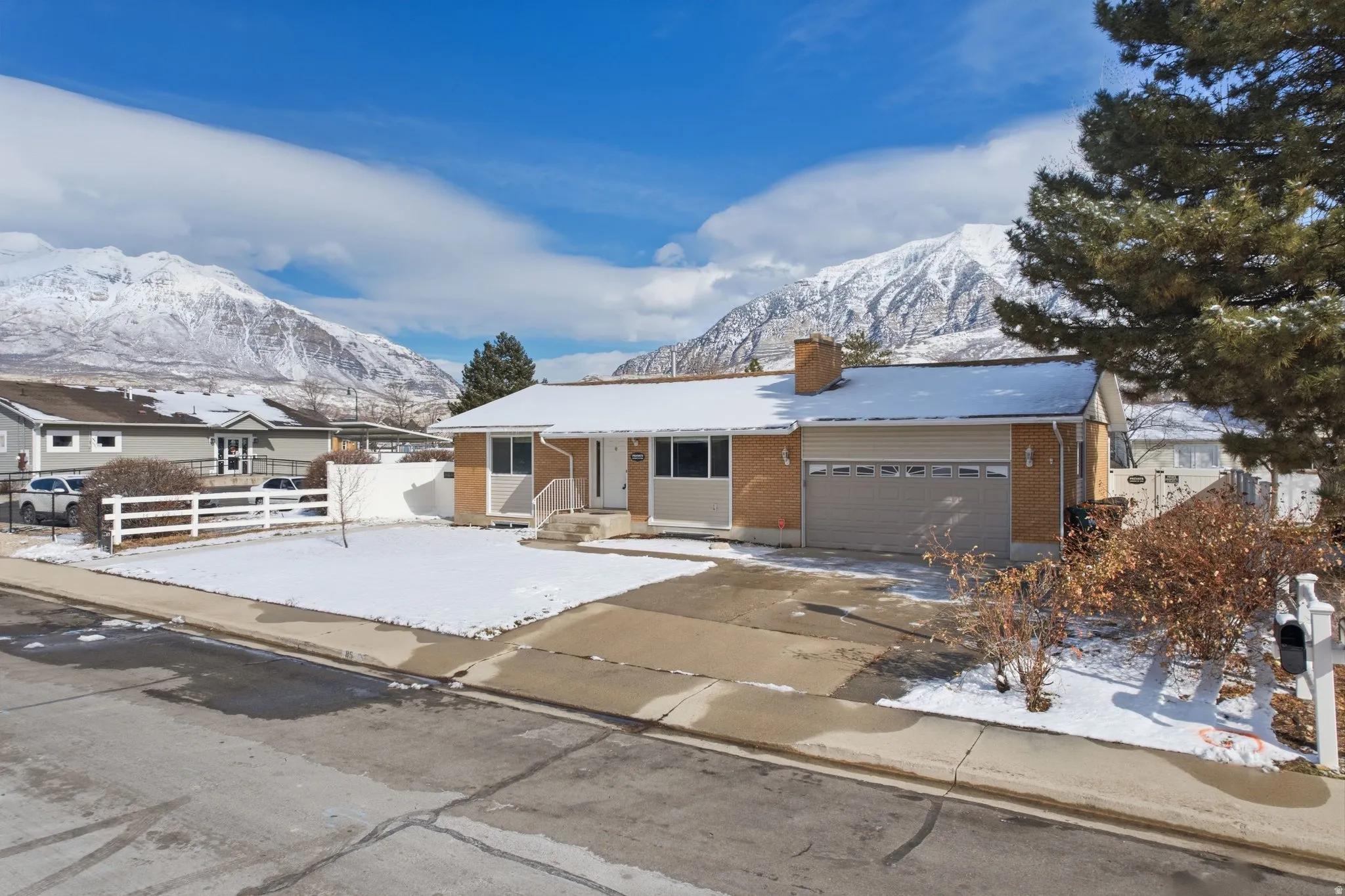 Single story home with brick siding, an attached garage, a mountain view, a chimney, and driveway