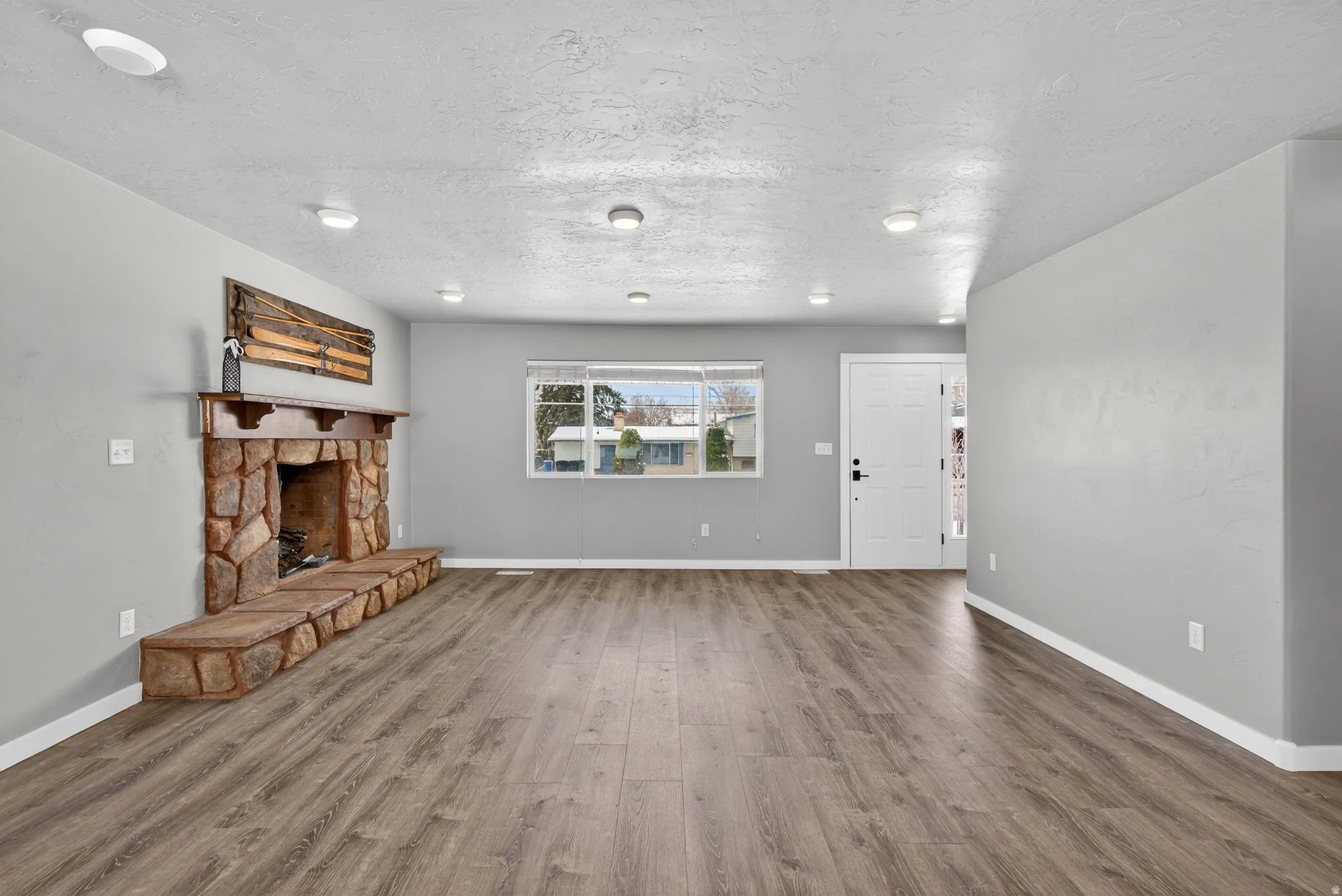 Unfurnished living room with wood finished floors, a stone fireplace, and a textured ceiling