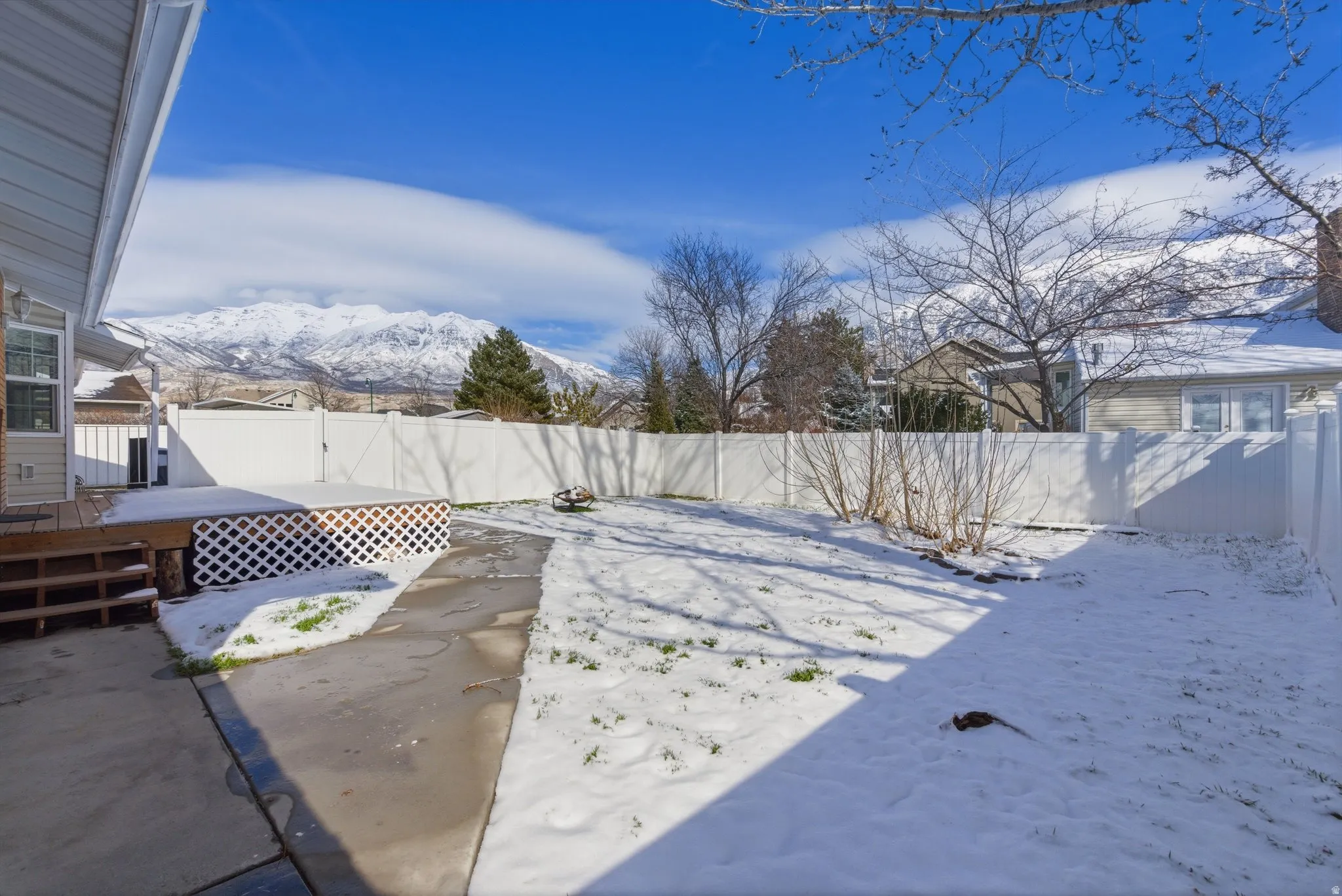 Snowy yard with a fenced backyard and a deck with mountain view