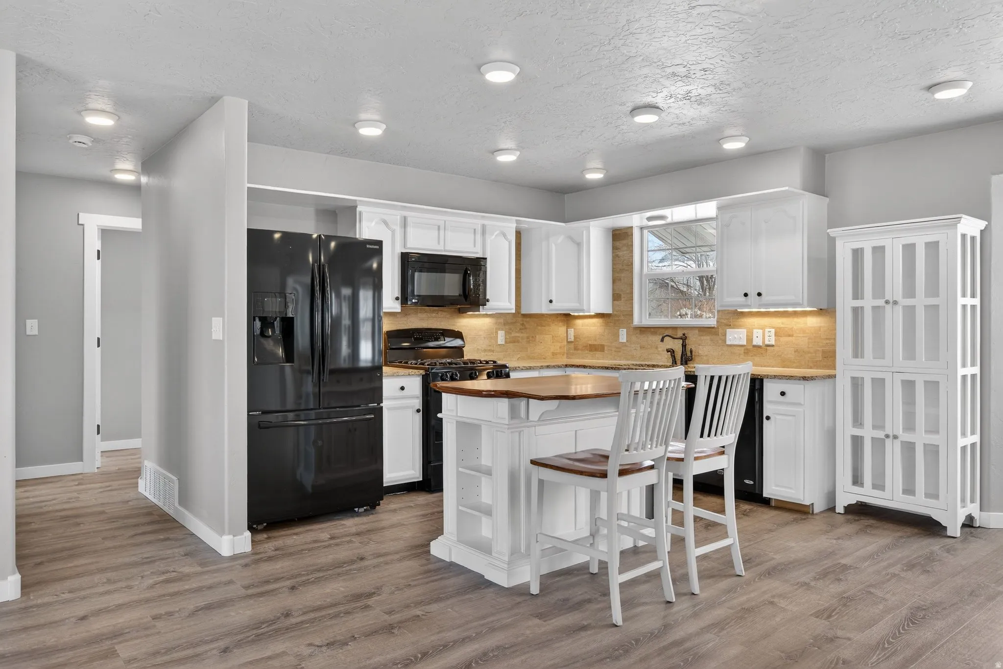 Kitchen featuring white cabinets, black appliances, a textured ceiling, a breakfast bar area, and light wood-style floors