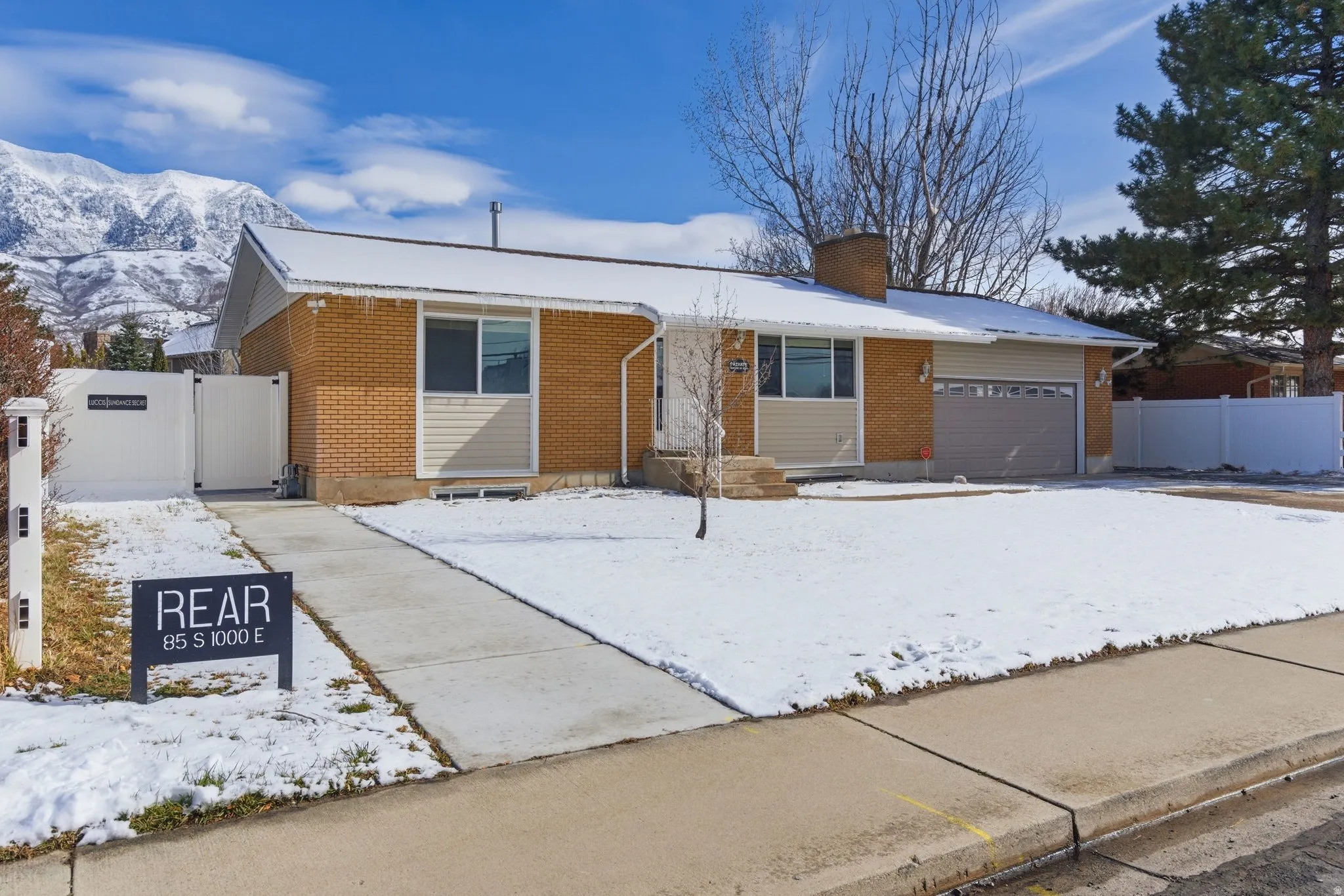 Ranch-style home featuring brick siding, a chimney, a gate, and a garage. Rear separate entrance to accessory apartment.
