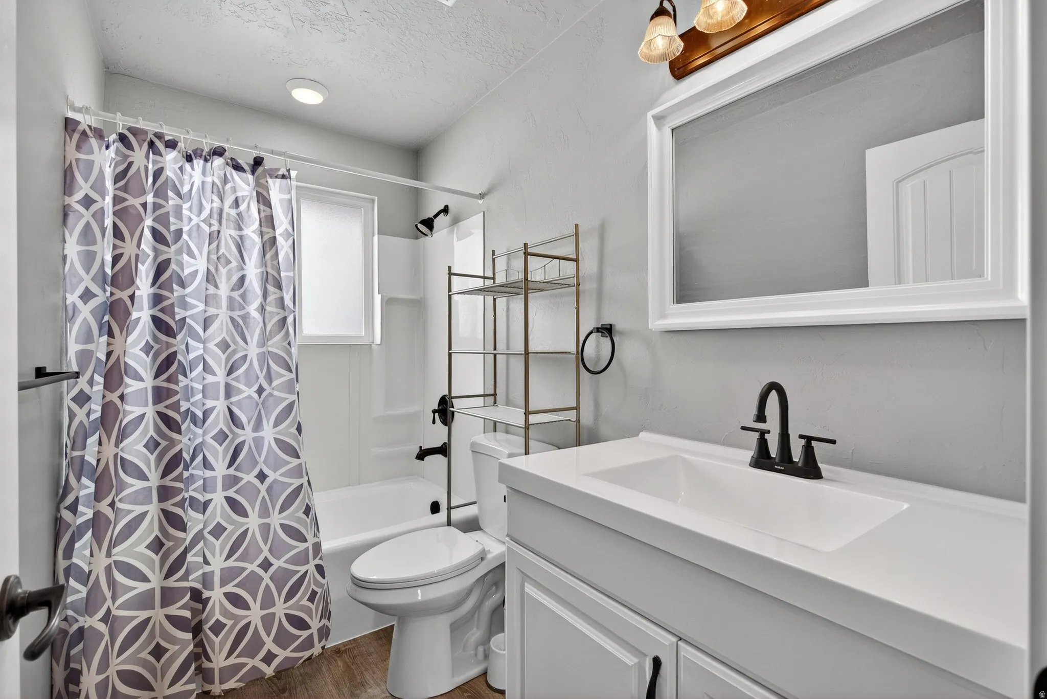Bathroom featuring vanity, shower / bathtub combination with curtain, dark wood-style floors, and a textured ceiling