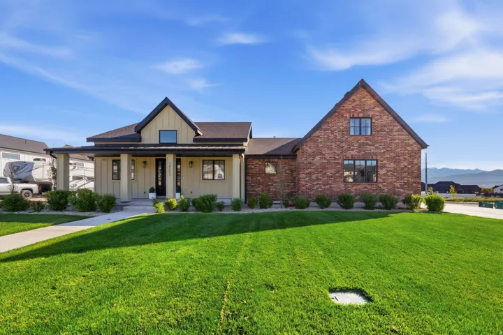 View of front of home with board and batten siding, covered porch, a front lawn, brick siding, and a mountain view