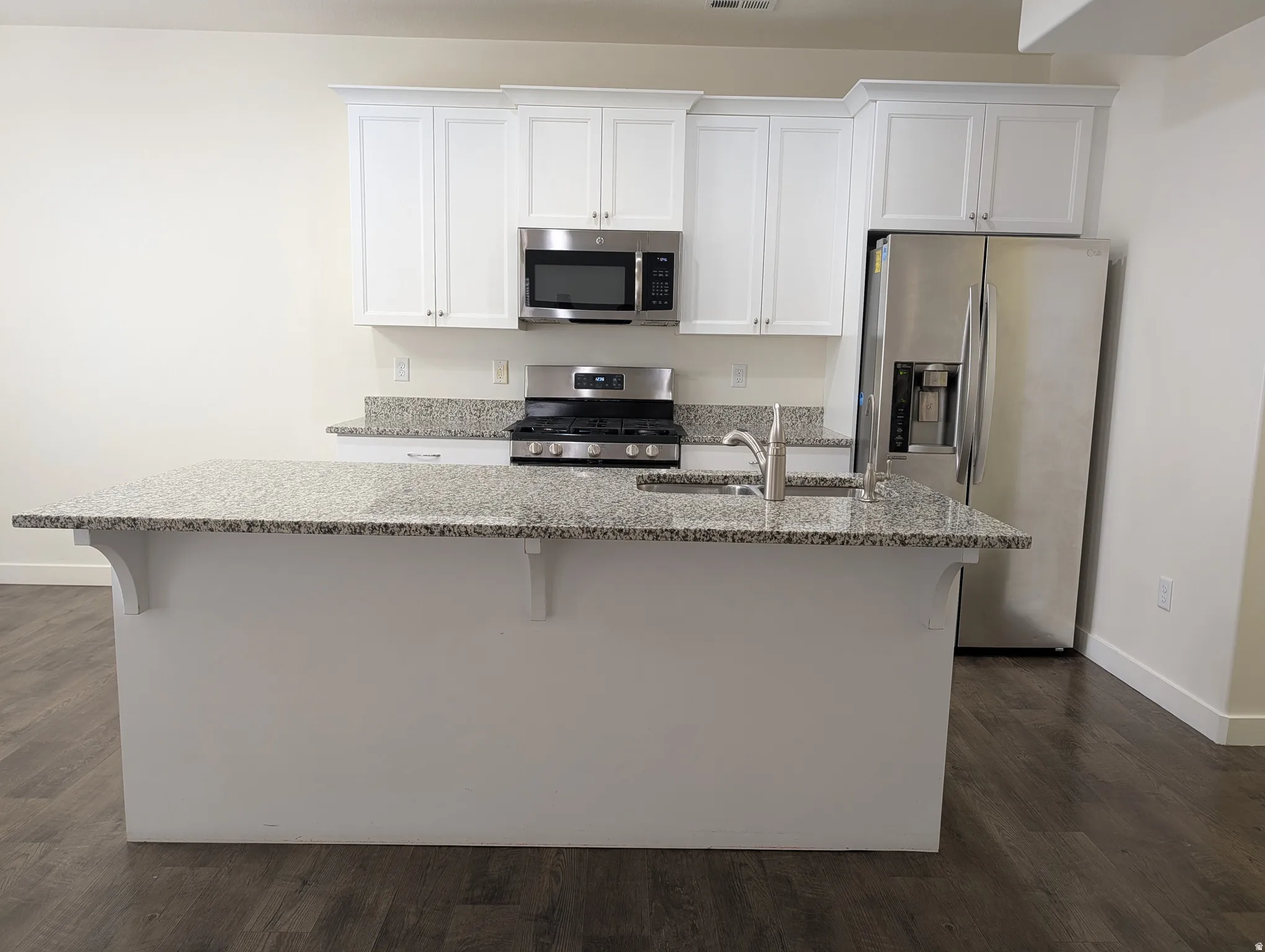 Kitchen with a breakfast bar area, stainless steel appliances, a kitchen island with sink, and white cabinets