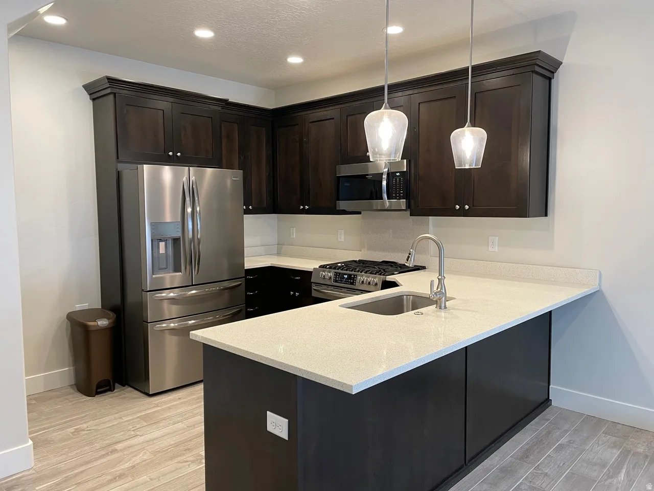 Kitchen with stainless steel appliances, decorative light fixtures, light stone counters, and dark wood finish cabinets