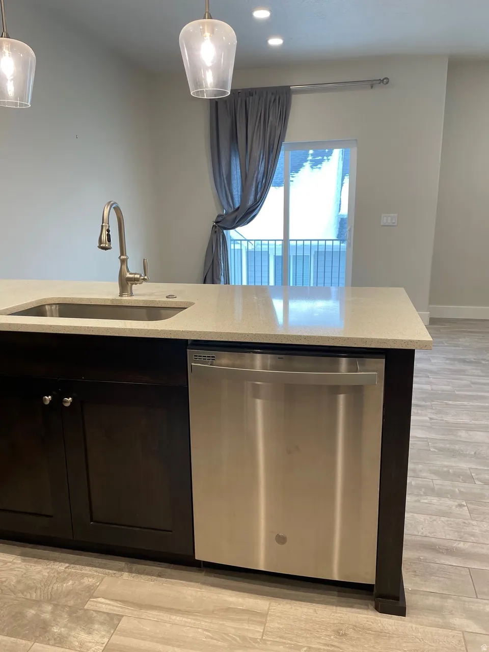 Kitchen with dishwasher, light wood-style floors, light stone counters, and dark cabinets