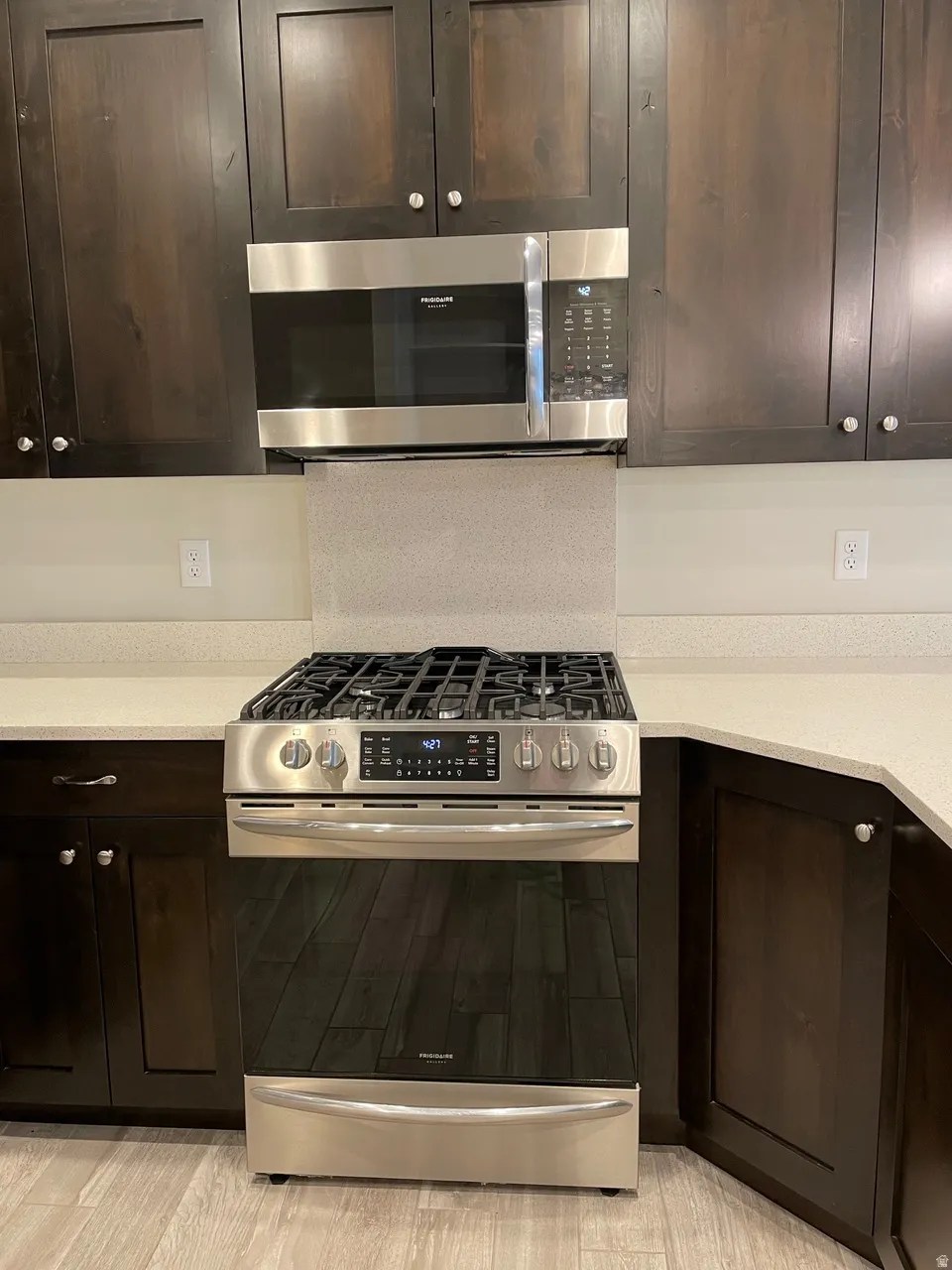 Kitchen featuring stainless steel appliances, dark wood finish cabinetry, and light stone counters