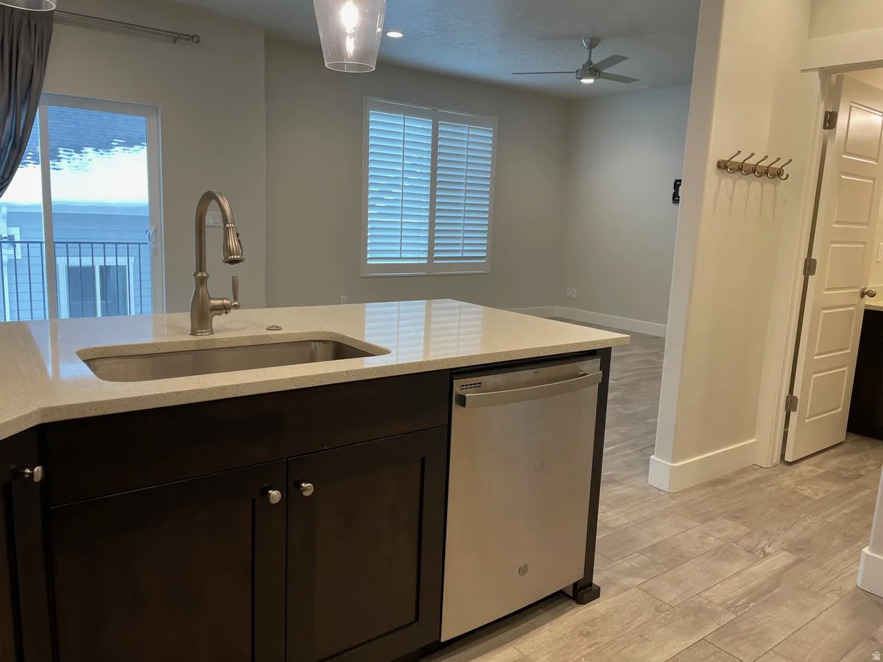 Kitchen with light wood-type flooring, dishwasher, dark wood finish cabinets, light stone counters, and a ceiling fan