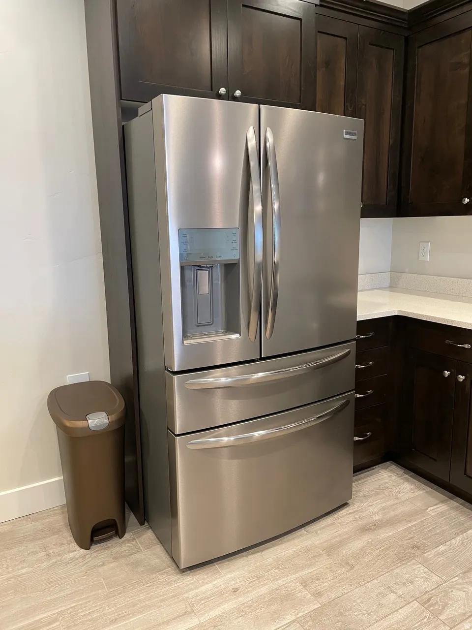 Kitchen featuring stainless steel refrigerator with ice dispenser, dark wood finish cabinetry, light wood finished floors, and light stone counters