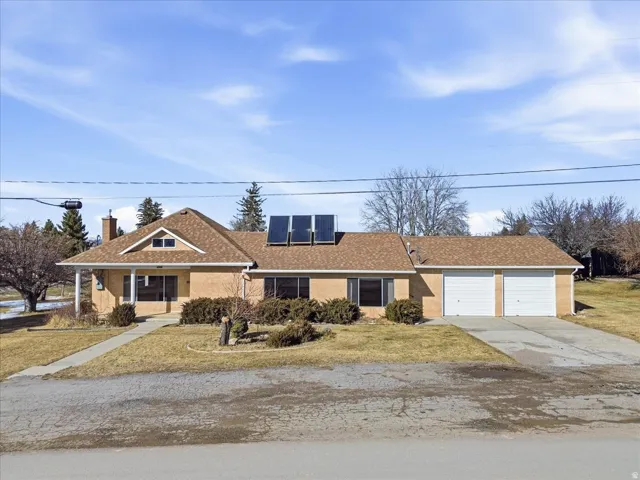 Ranch-style house with a front lawn, roof mounted solar panels, and driveway