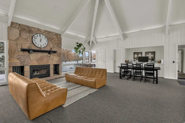 Living area with carpet flooring, a stone fireplace, and lofted ceiling