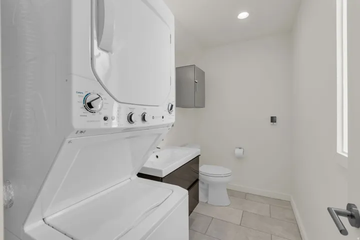 Bathroom with vanity, stacked washer and clothes dryer, light tile patterned flooring, and recessed lighting