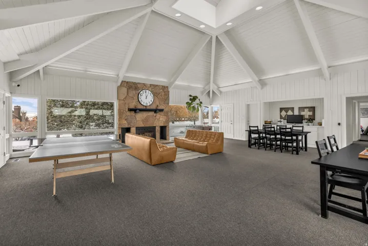 Carpeted living area featuring a stone fireplace, lofted ceiling, and wood walls