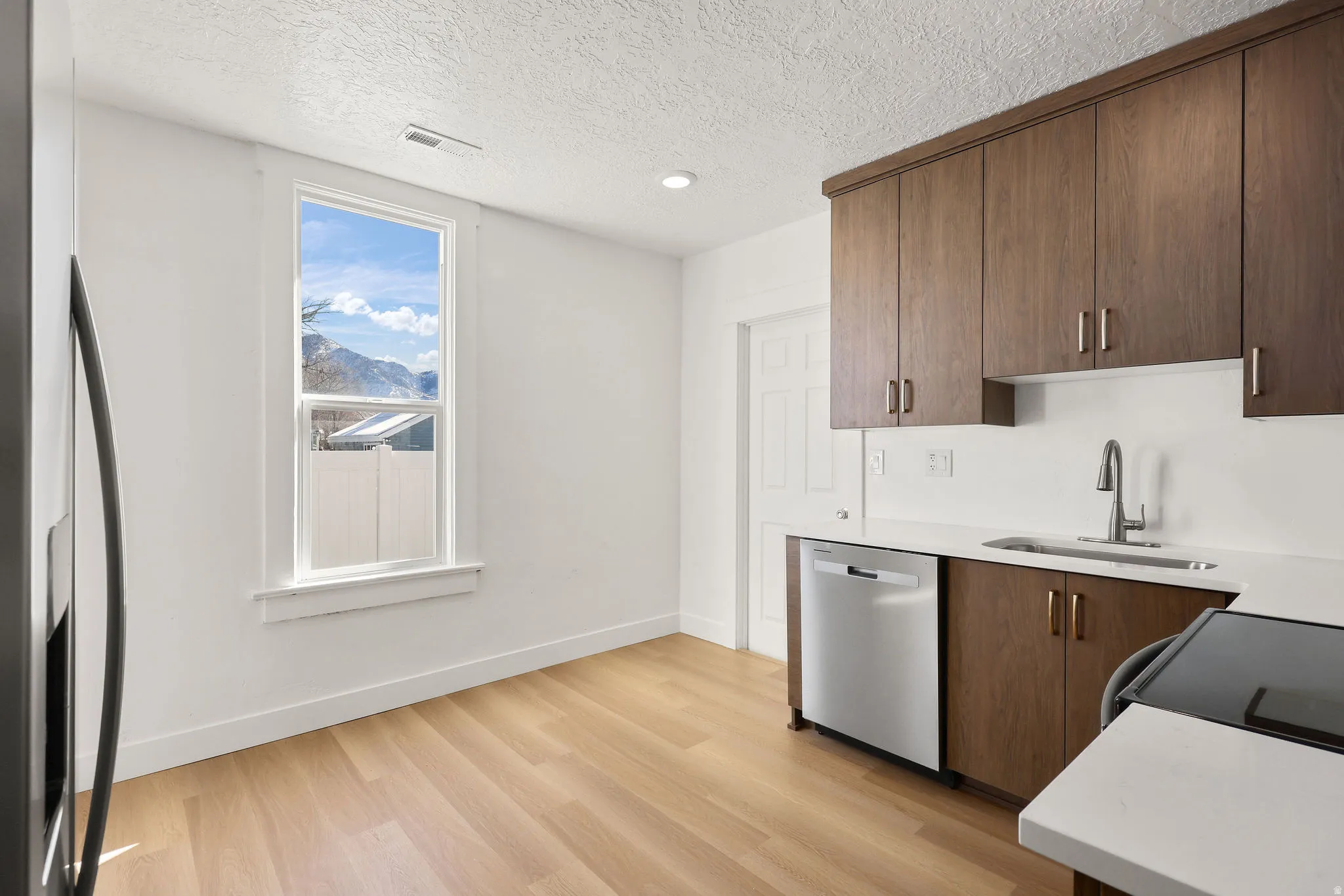 Kitchen featuring stainless steel appliances, light wood finished floors, light stone counters, a textured ceiling, and modern cabinets