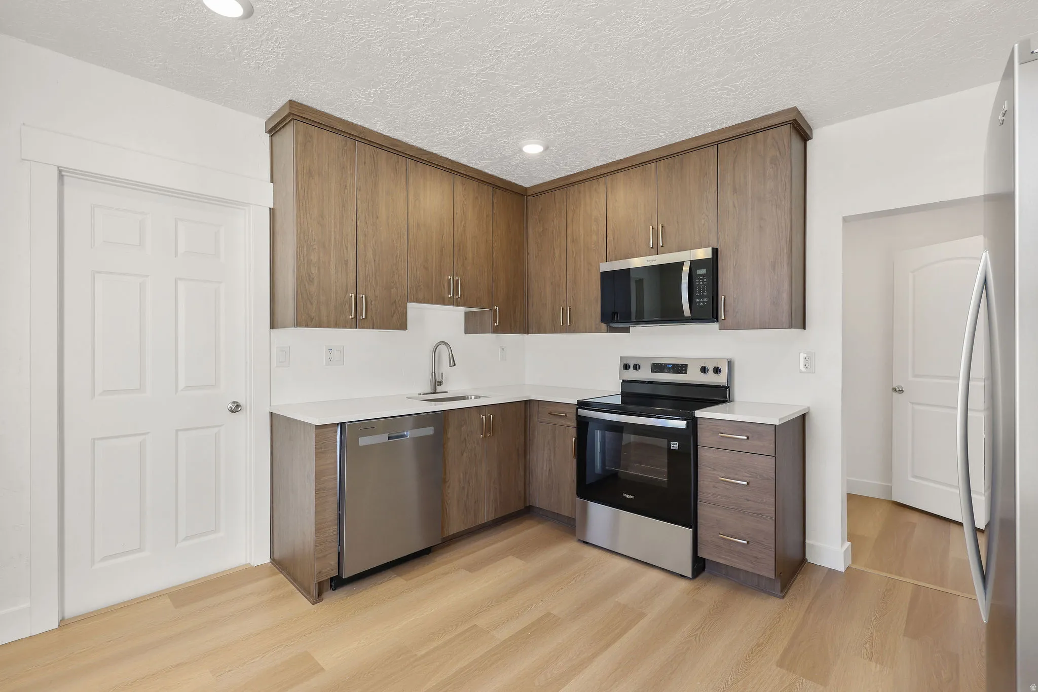 Kitchen featuring stainless steel appliances, modern cabinets, light wood-style flooring, recessed lighting, and light stone countertops