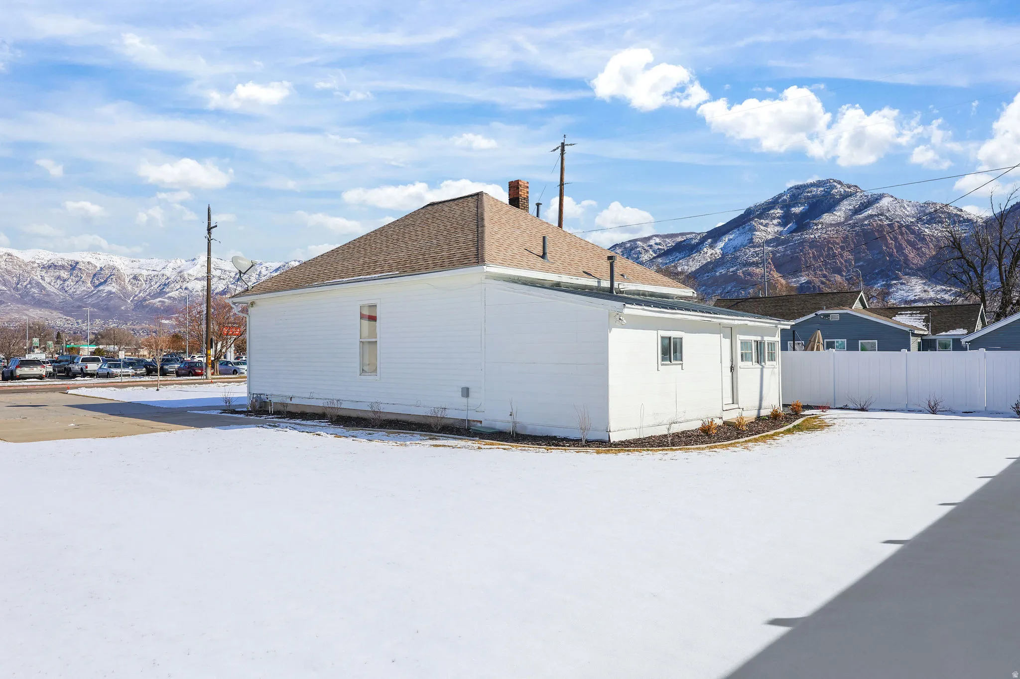 View of snowy exterior with a mountain view, a chimney, and roof with shingles