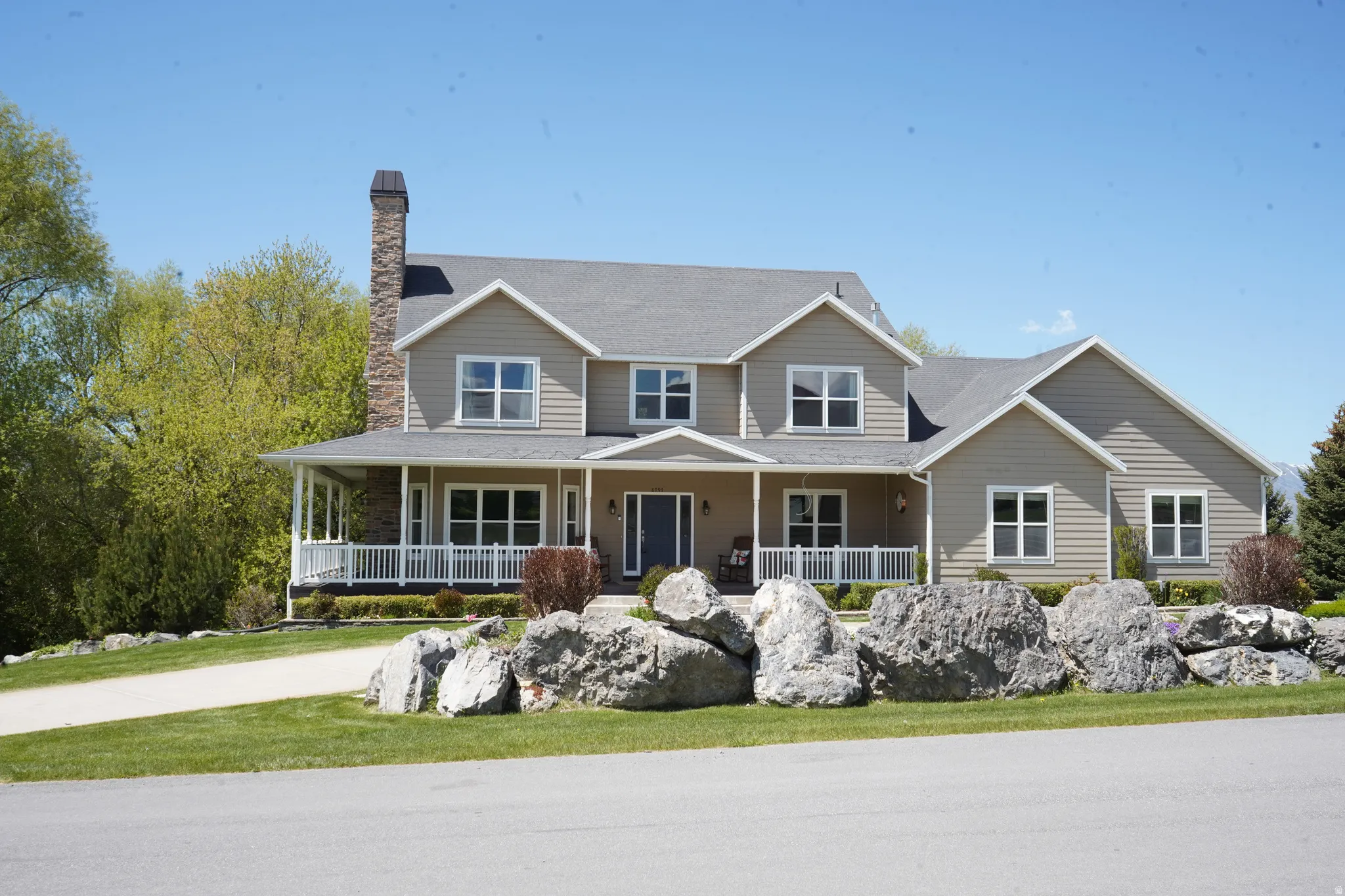 Two-story property featuring light tan siding, a dark gray roof, and a prominent stone chimney