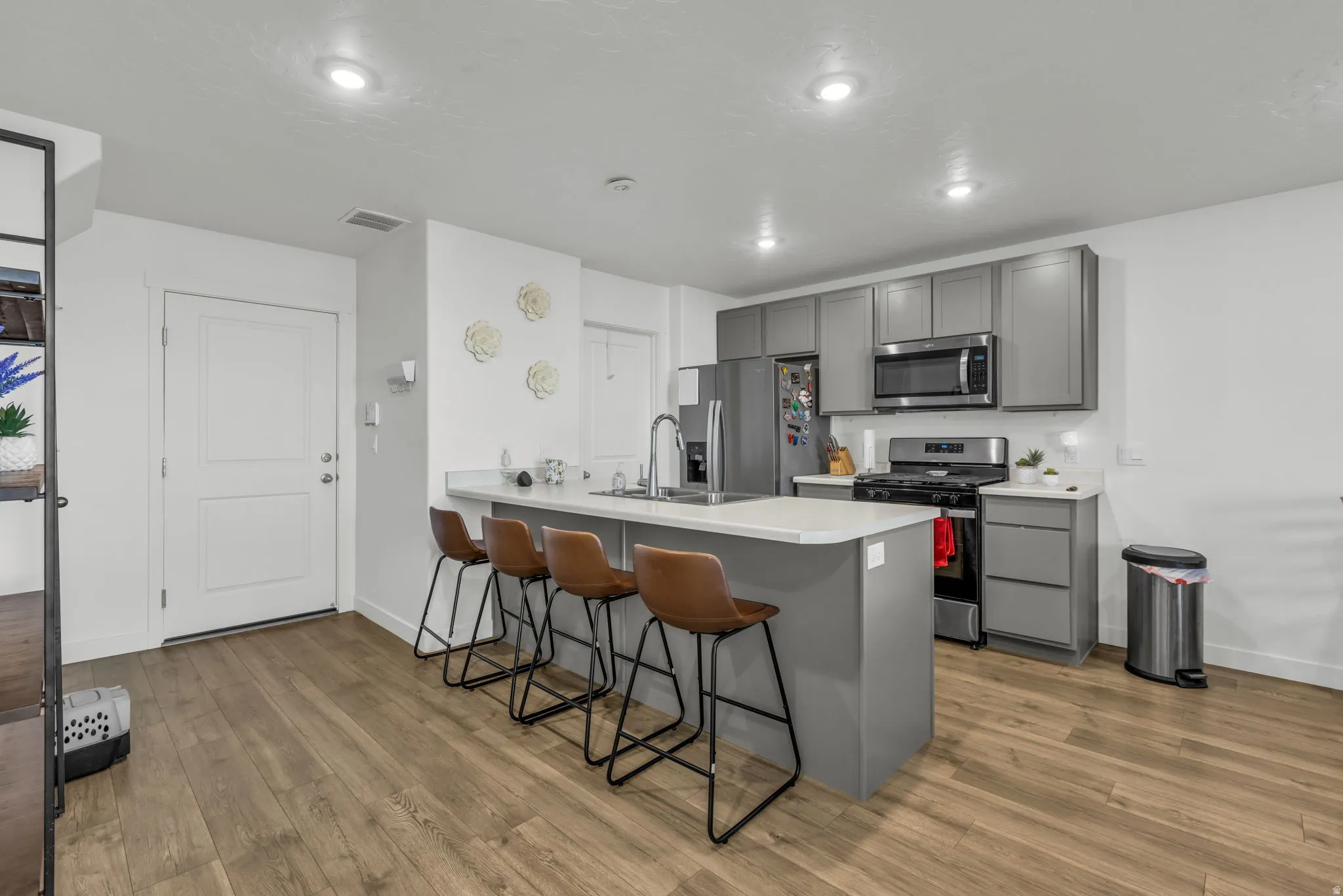 Kitchen with a breakfast bar, a peninsula, stainless steel appliances, gray cabinets, and light wood finished floors