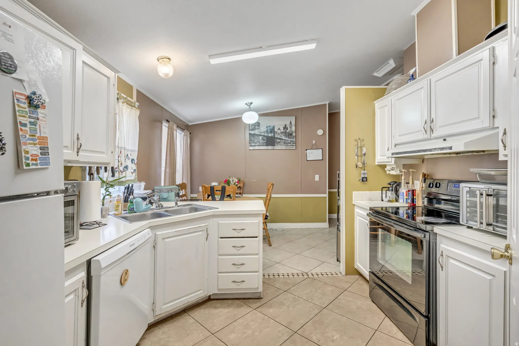 Kitchen featuring white appliances, a peninsula, white cabinetry, light countertops, and ornamental molding