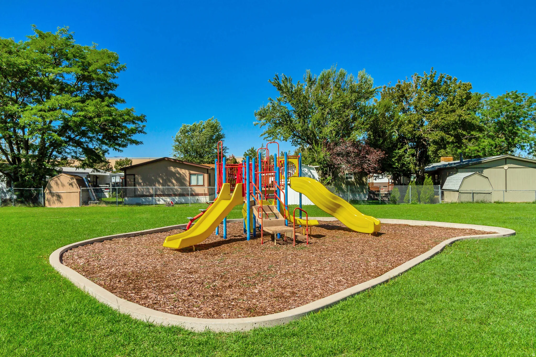 Grassed outdoor area featuring a playground with yellow slides and a wood chip base