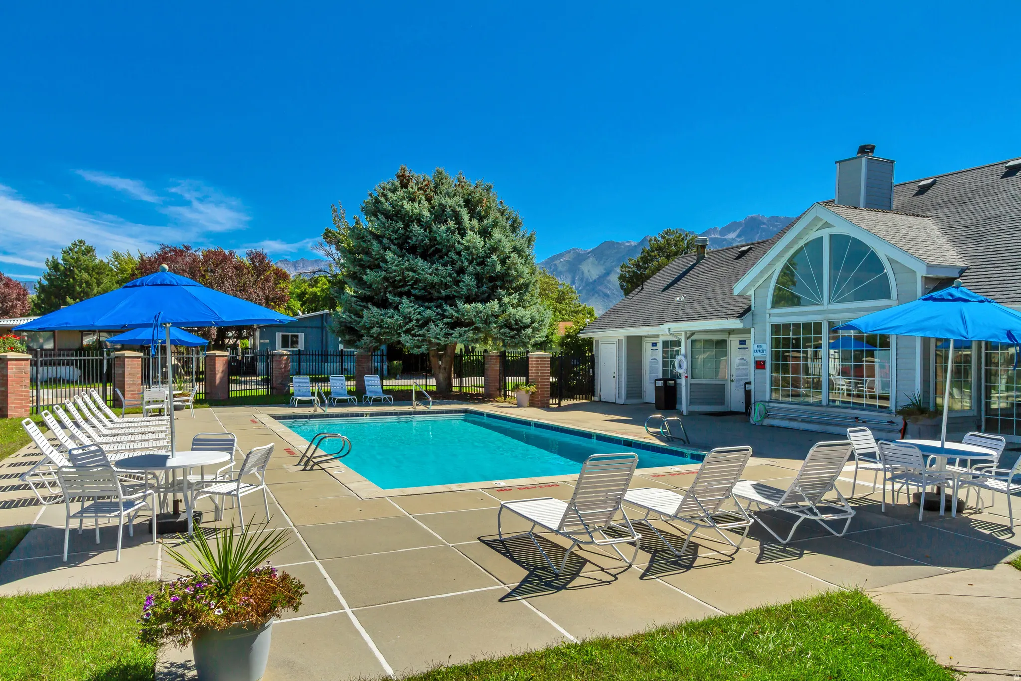 Resort-style outdoor pool with surrounding hardscaping, a building featuring a large arched window, and landscaped grounds with mature trees