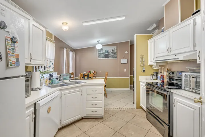 Kitchen featuring white appliances, a peninsula, white cabinetry, light countertops, and ornamental molding