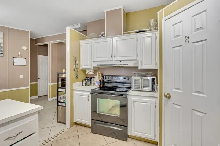 Kitchen featuring black electric range oven, white cabinetry, light tile patterned floors, and light countertops