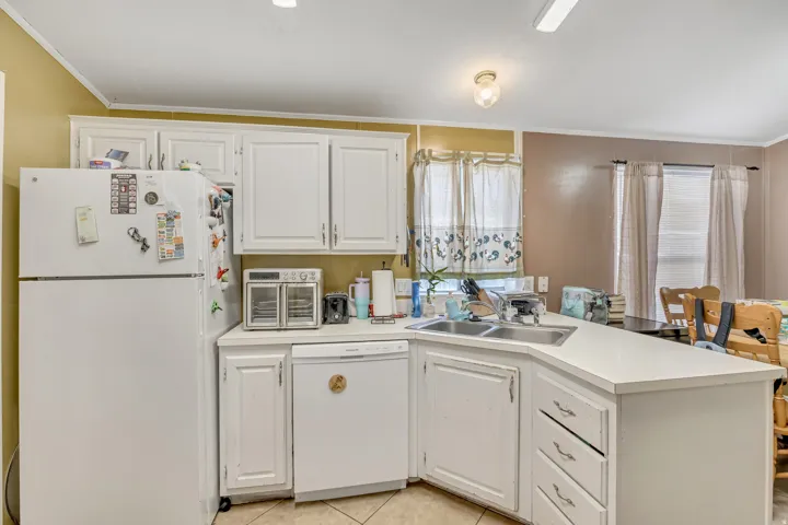 Kitchen featuring white appliances, light countertops, white cabinets, ornamental molding, and a peninsula