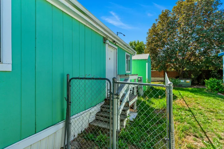 Exterior siding in a vibrant green finish, elevated wooden decking with stairs, a chain-link fence, and a separate storage shed
