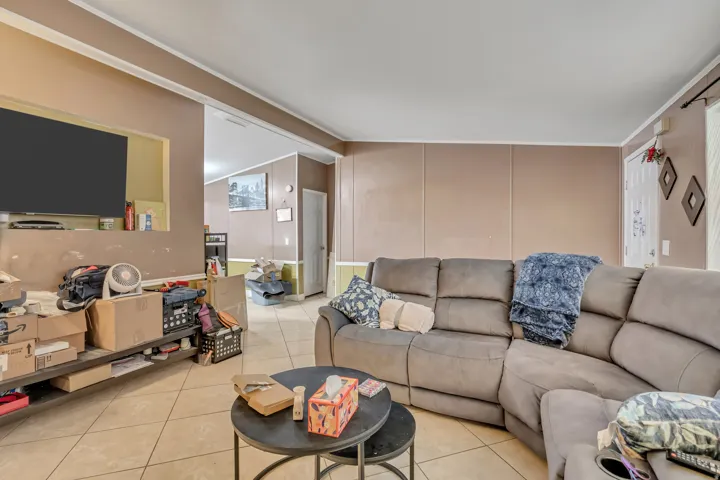 Living room with tile patterned flooring, lofted ceiling, a decorative wall, and crown molding
