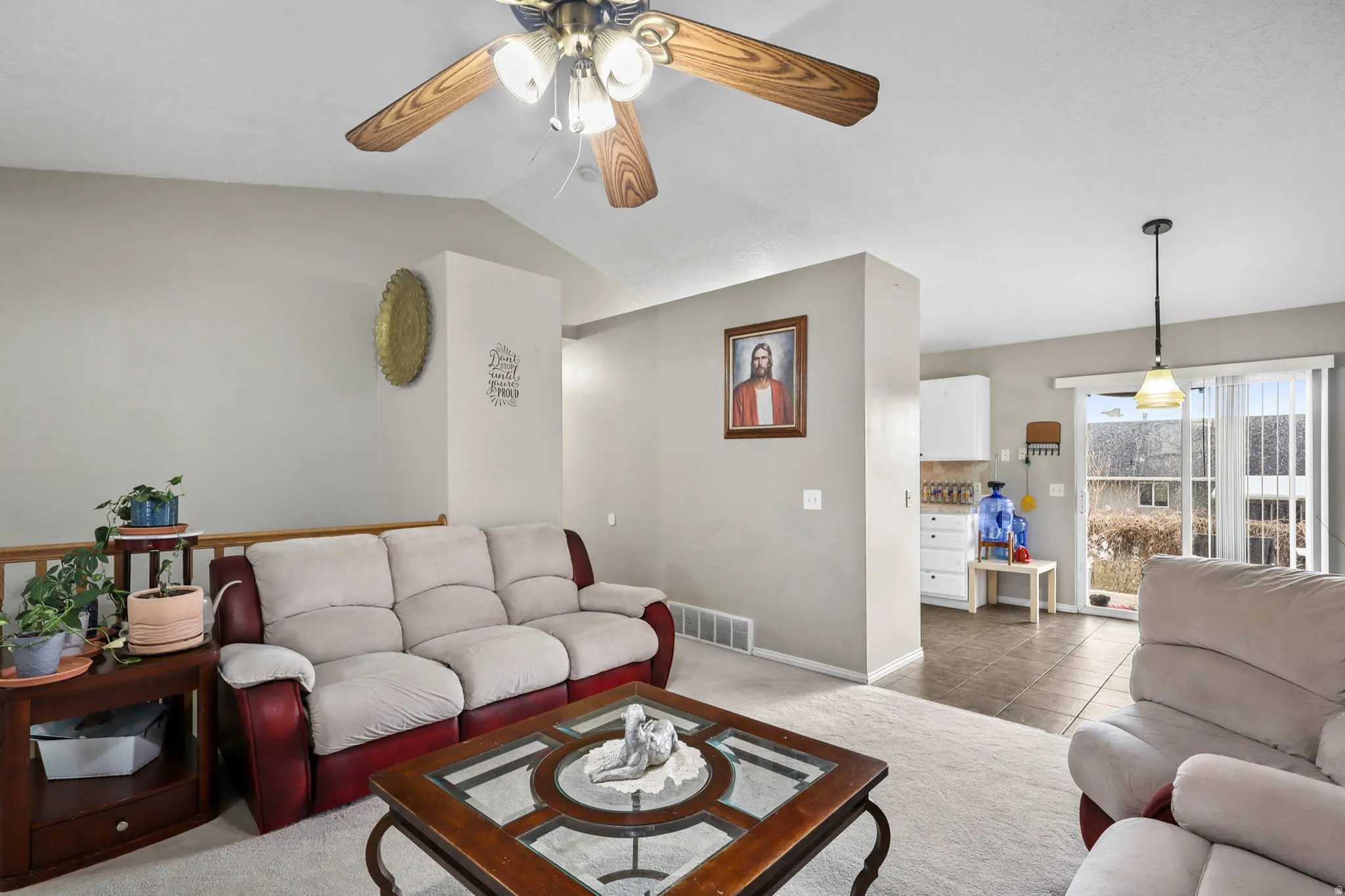 Tiled living area with a ceiling fan, vaulted ceiling, and carpet floors
