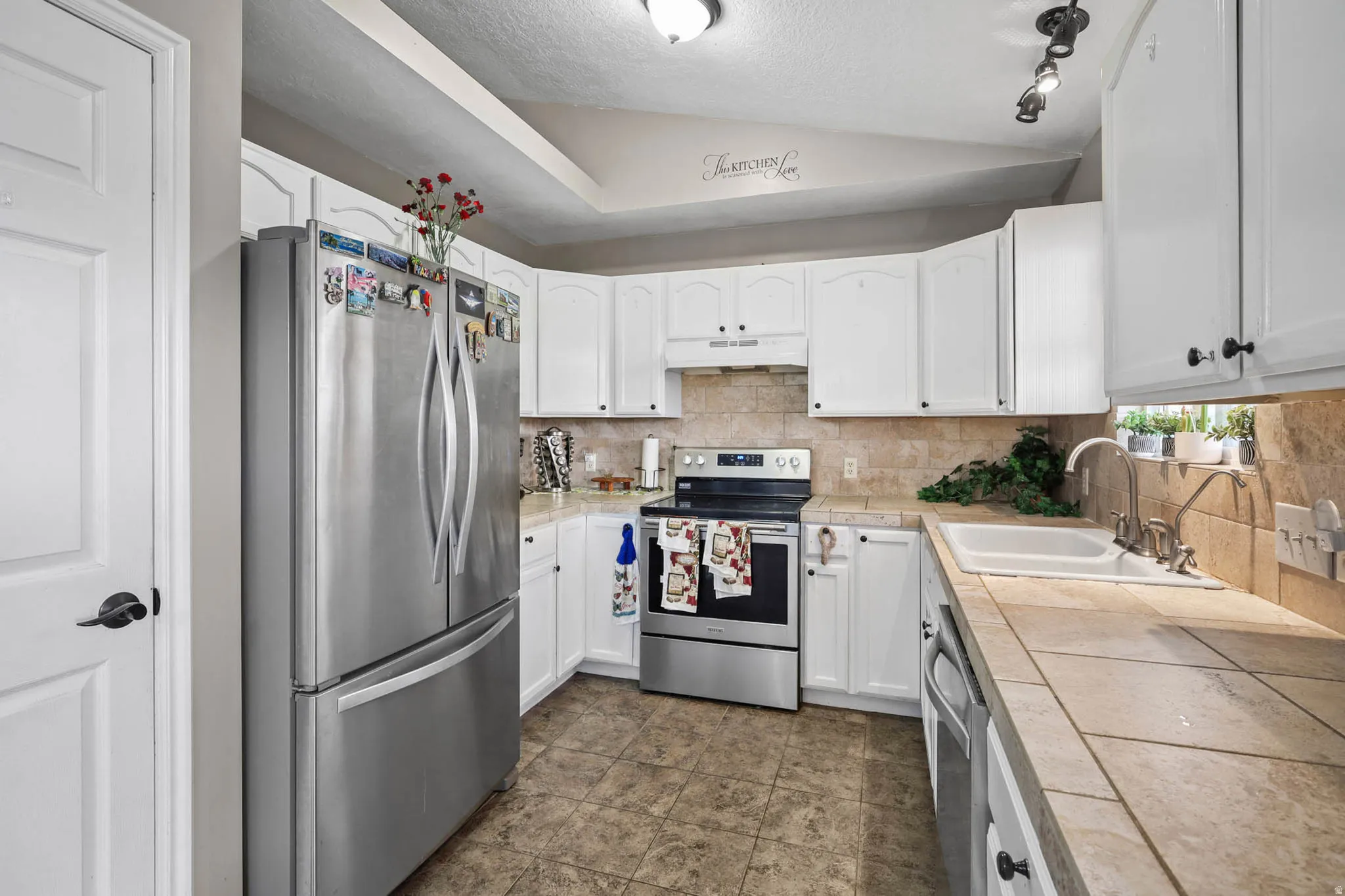 Kitchen featuring stainless steel appliances, white cabinetry, tasteful backsplash, and tile countertops